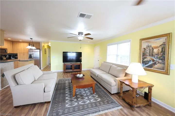 Living room featuring crown molding, ceiling fan, and light wood-style floors