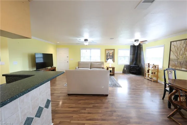 Living room with a wood stove, crown molding, dark wood-style flooring, and ceiling fan