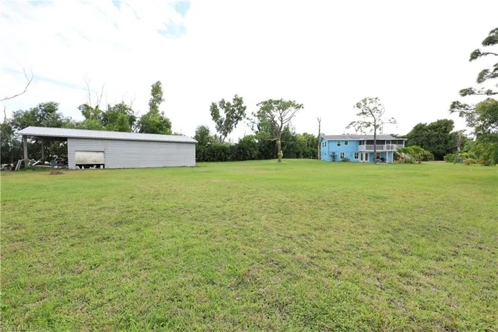 View of grassy yard featuring a pole building, an outdoor structure, and view of scattered trees