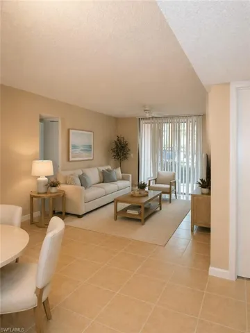 Open-concept living area featuring light-toned tile flooring, a sliding glass door with vertical blinds, and a neutral color palette #6