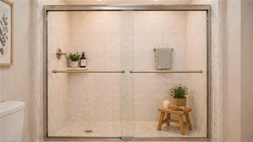 Glass-enclosed shower featuring light-toned tile walls, a coordinating tiled shower pan, a brushed nickel showerhead, and a matching towel bar