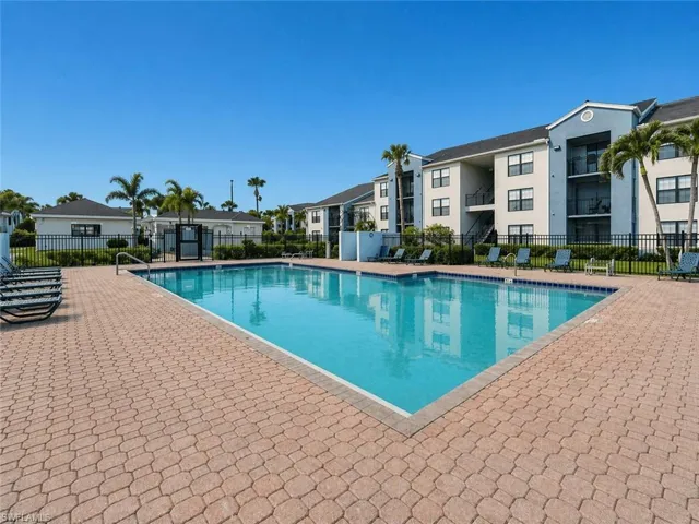 Outdoor swimming pool surrounded by paver decking, black metal fencing, and tropical landscaping