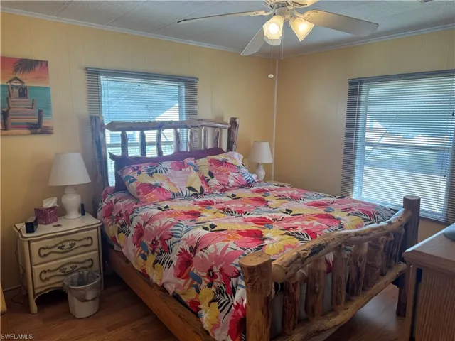 Bedroom featuring ornamental molding, wood finished floors, ceiling fan, multiple windows, and wooden walls