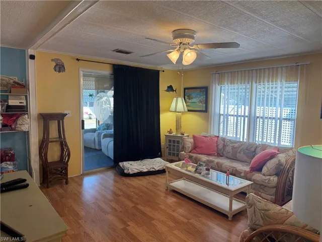 Living area featuring wood finished floors, healthy amount of natural light, a ceiling fan, and a textured ceiling