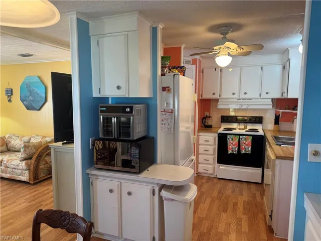 Kitchen featuring white appliances, white cabinetry, a textured ceiling, light countertops, and light wood-style flooring