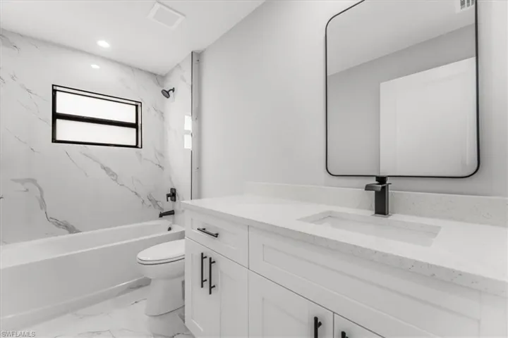Bathroom with marble look tiles, vanity, tub / shower combination, and recessed lighting