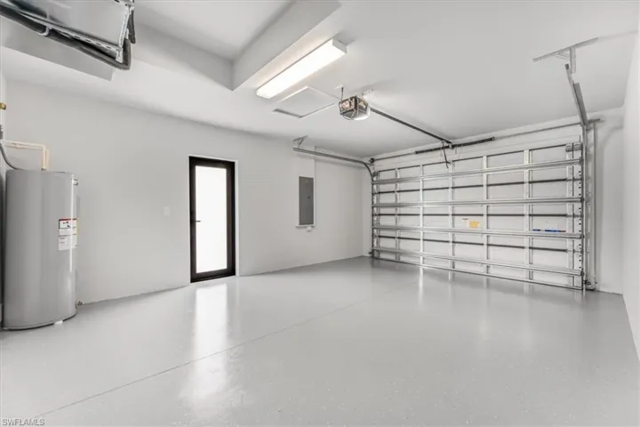 Garage with electric water heater, electric panel, and a garage door opener