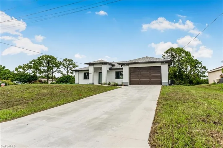 Prairie-style house featuring driveway, a garage, stucco siding, and a front lawn