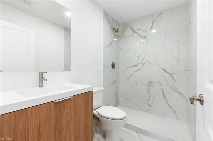 Full bath featuring vanity, toilet, a marble finish shower, and visible vents