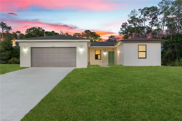 View of front of house with an attached garage, a front lawn, stucco siding, and concrete driveway