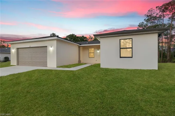 View of front of home featuring a garage, stucco siding, driveway, and a front yard