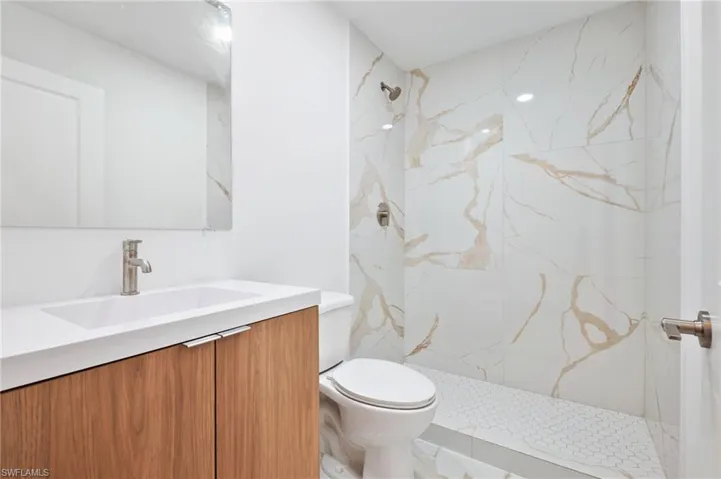 Bathroom with vanity, a marble finish shower, and toilet