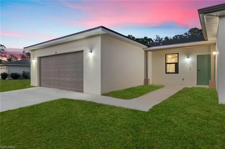Property exterior at dusk with a lawn, stucco siding, and concrete driveway