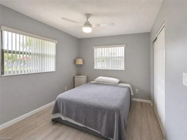 Bedroom featuring neutral wall colors, wood-finish flooring, two windows with vertical blinds, a ceiling fan with integrated lighting, and a bi-fold closet door