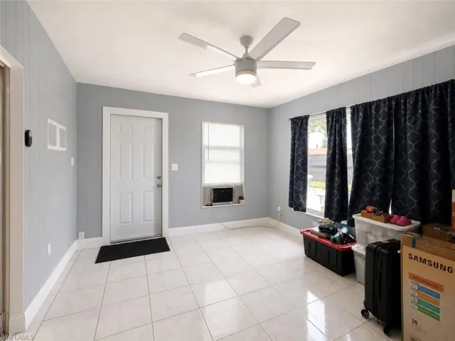 Spacious room featuring white tile flooring, light gray vertical paneling, and a contemporary ceiling fan with integrated lighting