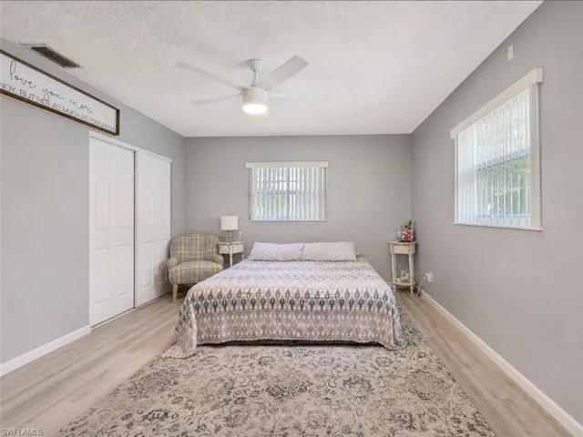 Spacious room featuring light wood-finish flooring, two large windows with vertical blinds, and a ceiling fan