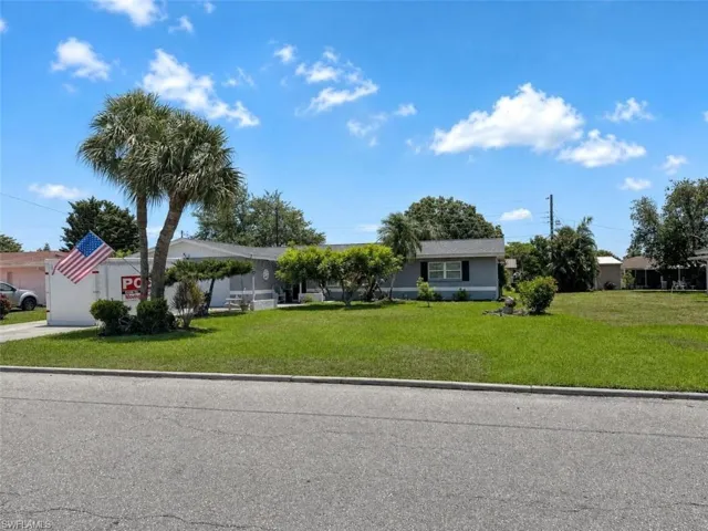 Single-story residence featuring a well-maintained lawn and mature palm trees