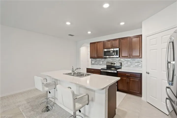 Kitchen with a center island with sink, appliances with stainless steel finishes, sink, light tile patterned floors, and decorative backsplash