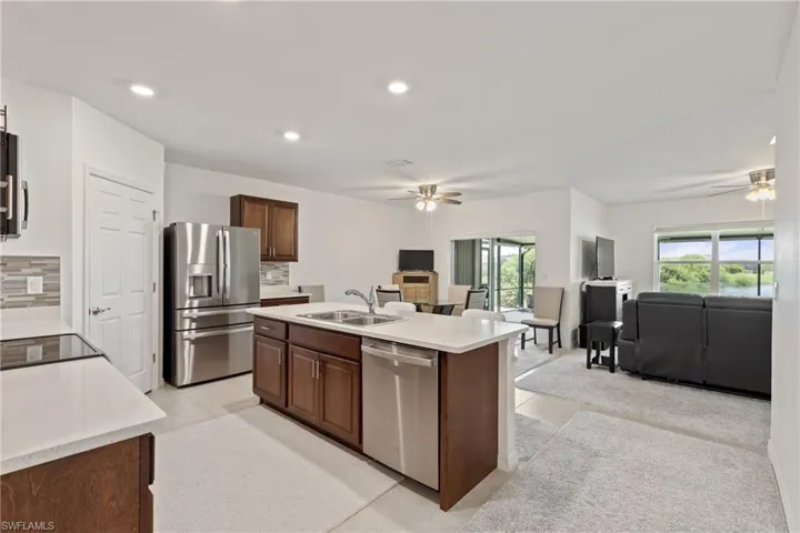 Kitchen with light tile patterned floors, appliances with stainless steel finishes, a kitchen island with sink, ceiling fan, and decorative backsplash