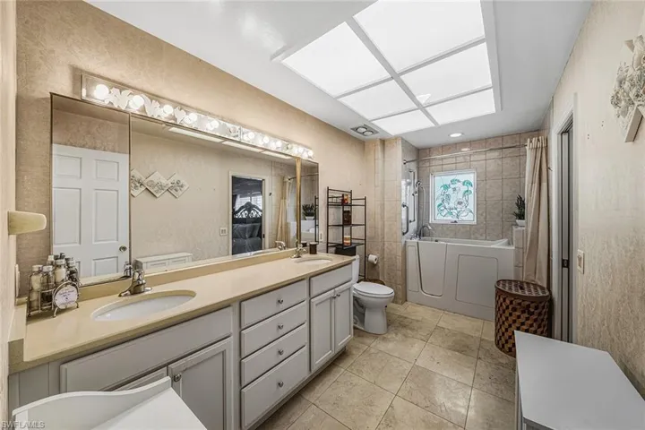 Bathroom featuring double vanity, a bath, light tile patterned floors, a shower with shower curtain, and a textured wall