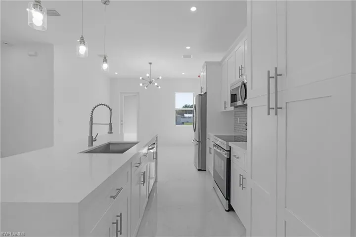 Kitchen with white cabinetry, stainless steel appliances, an inviting chandelier, a kitchen island with sink, and sink