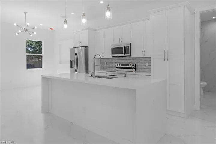 Kitchen with sink, white cabinets, a center island with sink, appliances with stainless steel finishes, and decorative light fixtures