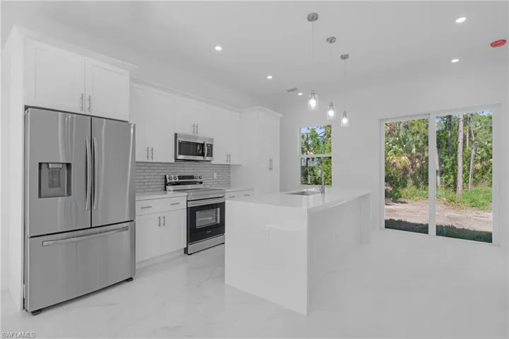 Kitchen featuring white cabinets, pendant lighting, a center island with sink, backsplash, and appliances with stainless steel finishes