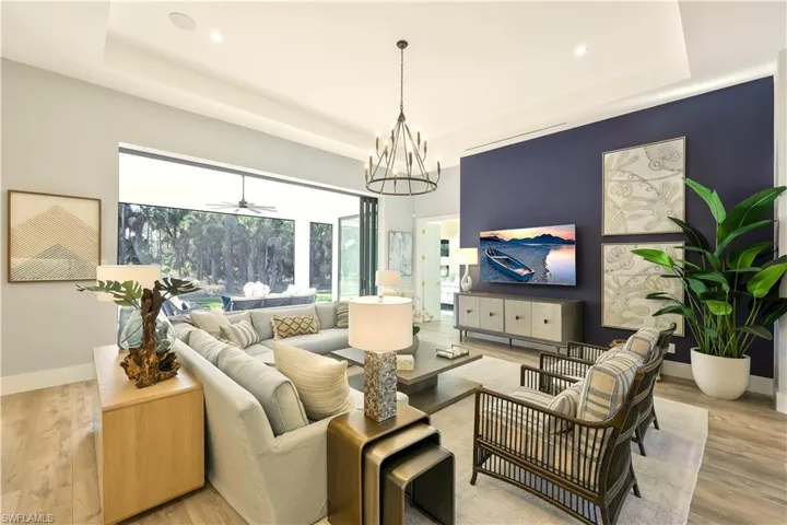 Living area with light wood-style floors, a chandelier, a raised ceiling, and a ceiling fan