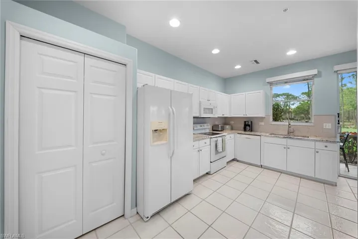 Kitchen with white appliances, white cabinetry, backsplash, light stone counters, and recessed lighting
