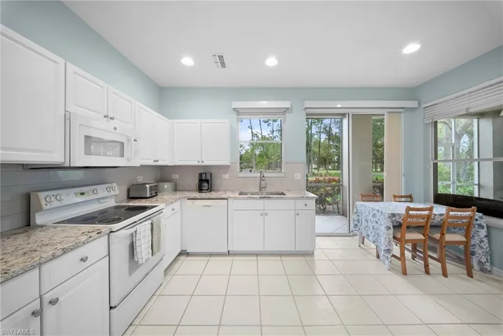 Kitchen with white appliances, light stone countertops, decorative backsplash, white cabinets, and recessed lighting