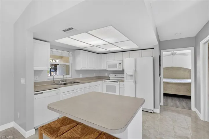 Kitchen featuring white appliances, white cabinetry, light countertops, a center island, and a breakfast bar