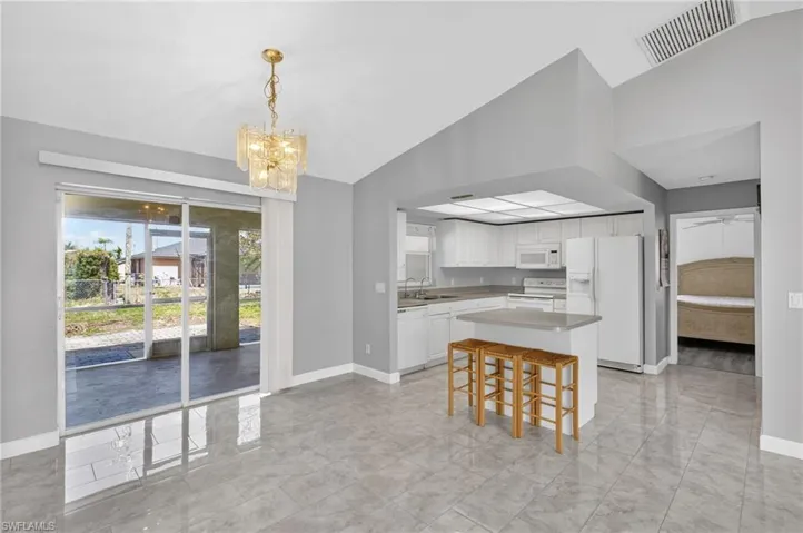Kitchen featuring white appliances, vaulted ceiling, white cabinetry, light countertops, and hanging lights