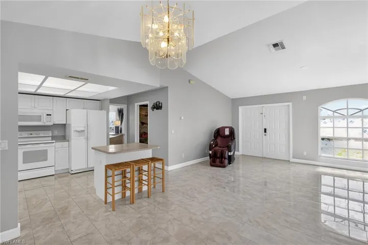 Kitchen featuring white appliances, white cabinetry, a kitchen breakfast bar, a chandelier, and open floor plan
