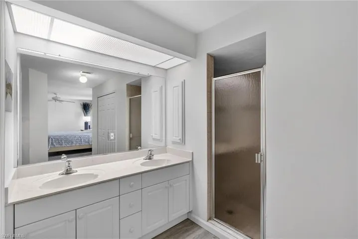 Ensuite bathroom with double vanity, a stall shower, ceiling fan, and light wood finished floors