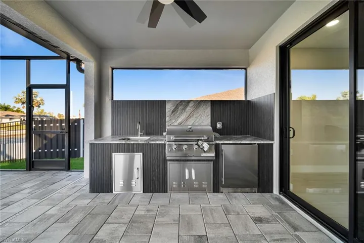 View of patio featuring exterior kitchen, a sunroom, ceiling fan, and a gate