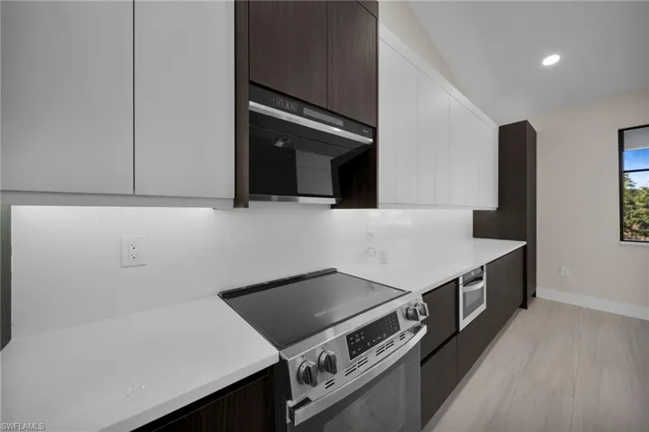 Dual tone kitchen featuring two tone color scheme, modern cabinets, stainless steel range with electric stovetop, black microwave, and recessed lighting