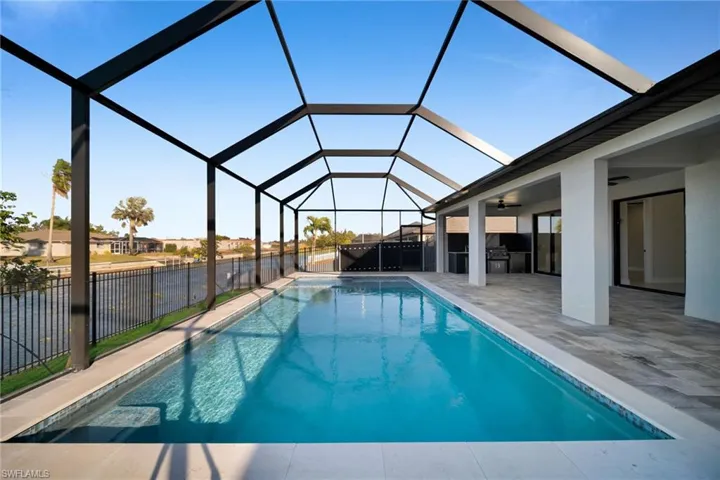 View of pool with exterior kitchen, glass enclosure, a sunroom, and patio surround