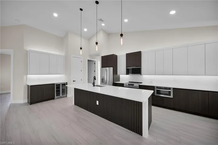 Kitchen featuring two tone cabinets, modern cabinets, decorative light fixtures, a center island with sink, and beverage cooler
