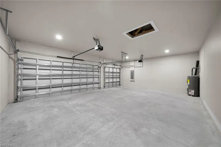 Garage featuring electric water heater, electric panel, recessed lighting, and a garage door opener
