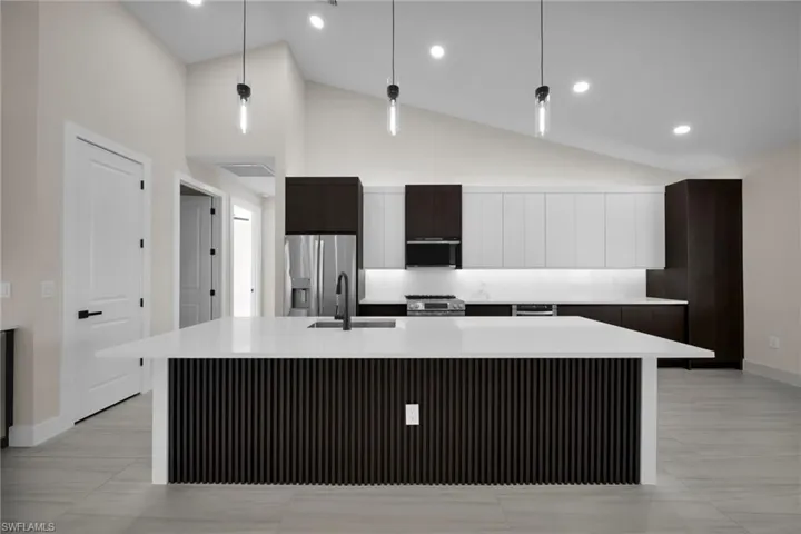 Kitchen featuring modern cabinets, a center island with sink, vaulted ceiling, decorative light fixtures, and stainless steel appliances