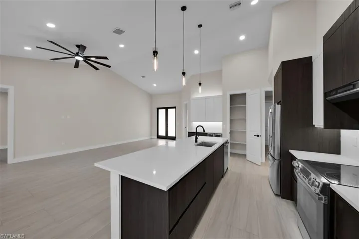 Kitchen featuring dark wood finish cabinets, modern cabinets, an island with sink, stainless steel appliances, and lofted ceiling