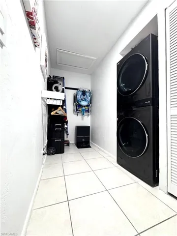 Laundry area with stacked washer and dryer and light tile patterned floors