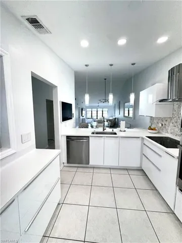 Kitchen with white cabinets, open floor plan, decorative light fixtures, and stainless steel dishwasher