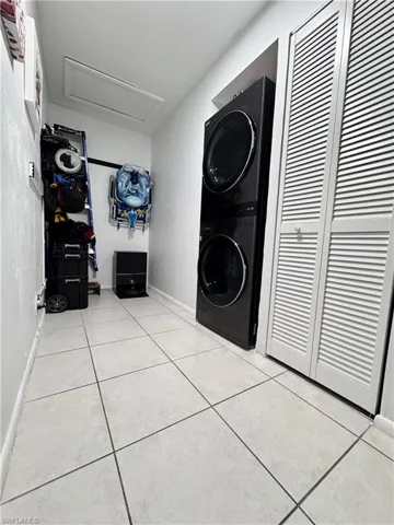 Laundry area with stacked washer / drying machine and light tile patterned flooring