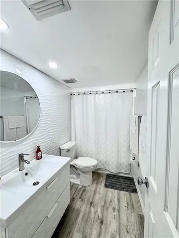 Bathroom featuring vanity, shower / tub combo, light wood-style flooring, recessed lighting, and tile walls