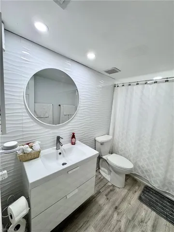 Bathroom with curtained shower, vanity, tile walls, wood finished floors, and recessed lighting
