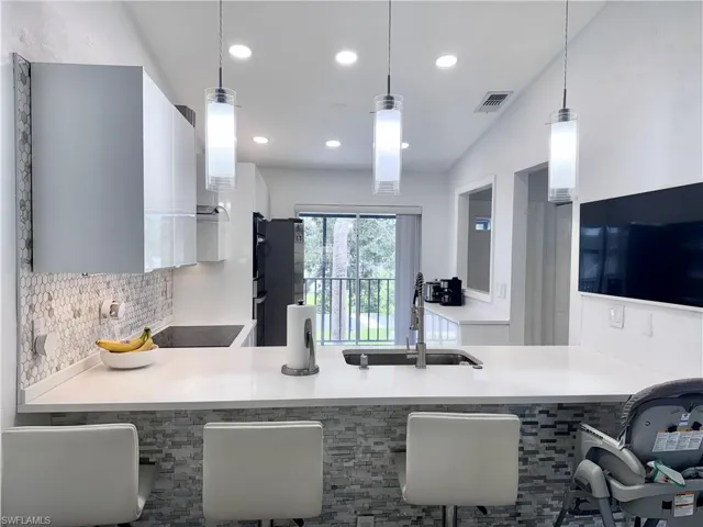 Kitchen with white cabinetry, a peninsula, hanging light fixtures, black electric cooktop, and modern cabinets