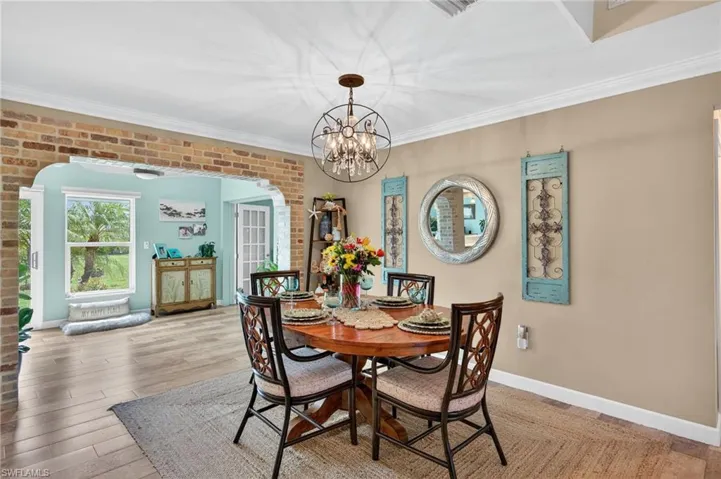 Dining space with arched walkways, a chandelier, crown molding, and wood finished floors