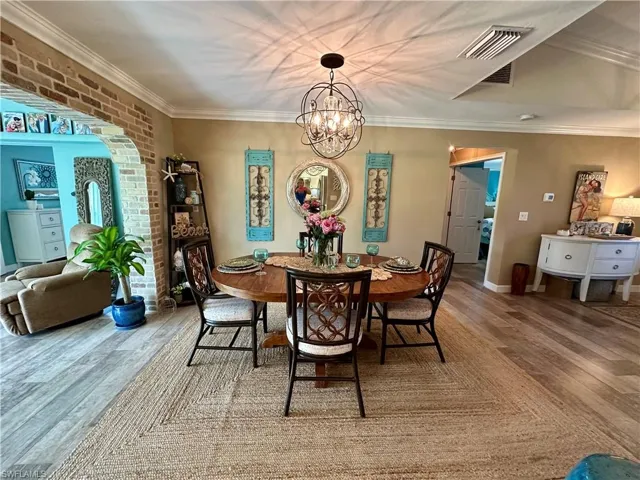 Dining area with crown molding, a chandelier, wood finished floors, arched walkways, and brick wall