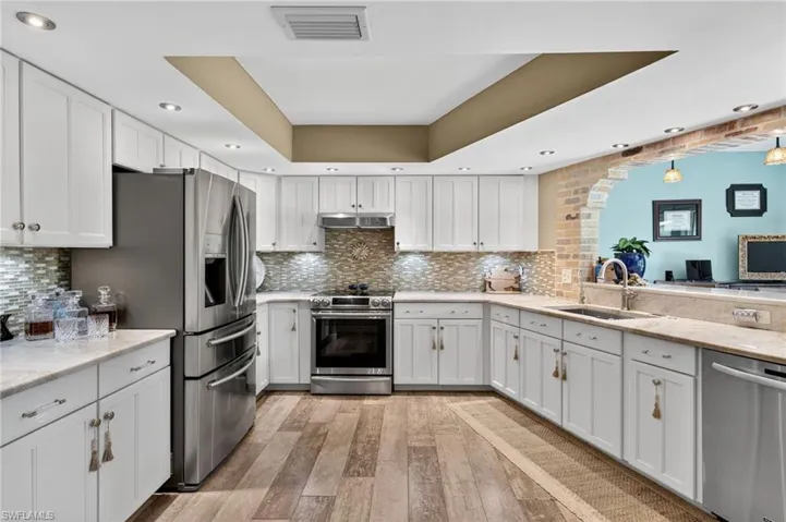 Kitchen with stainless steel appliances, recessed lighting, light wood-style floors, a raised ceiling, and white cabinetry